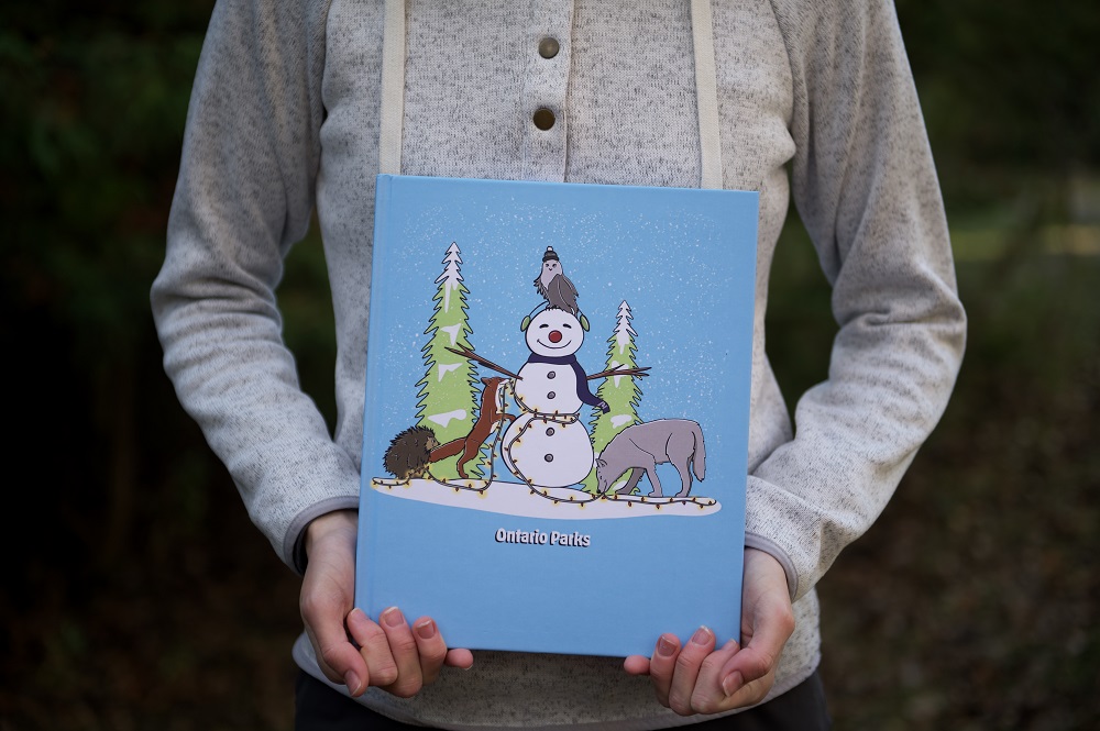 sketchbook with snowman and wildlife held in person's hands