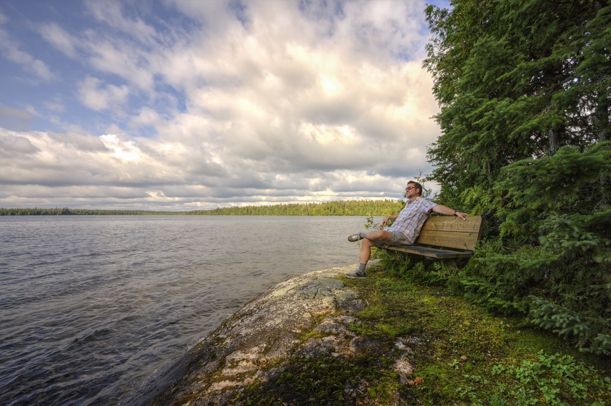 Man on bench watching lake and sky
