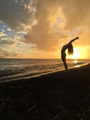 Woman does backbend on beach during sunset