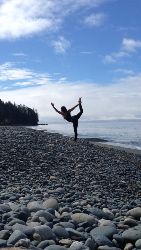 Woman does yoga pose on rocky beach