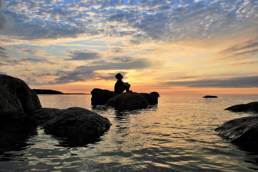 Un enfant assis sur une roche dans l'eau regarde le coucher de soleil