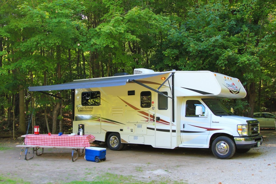 Une autocaravane OWASCO installée à l’emplacement de camping avec une table de pique-nique et un auvent 