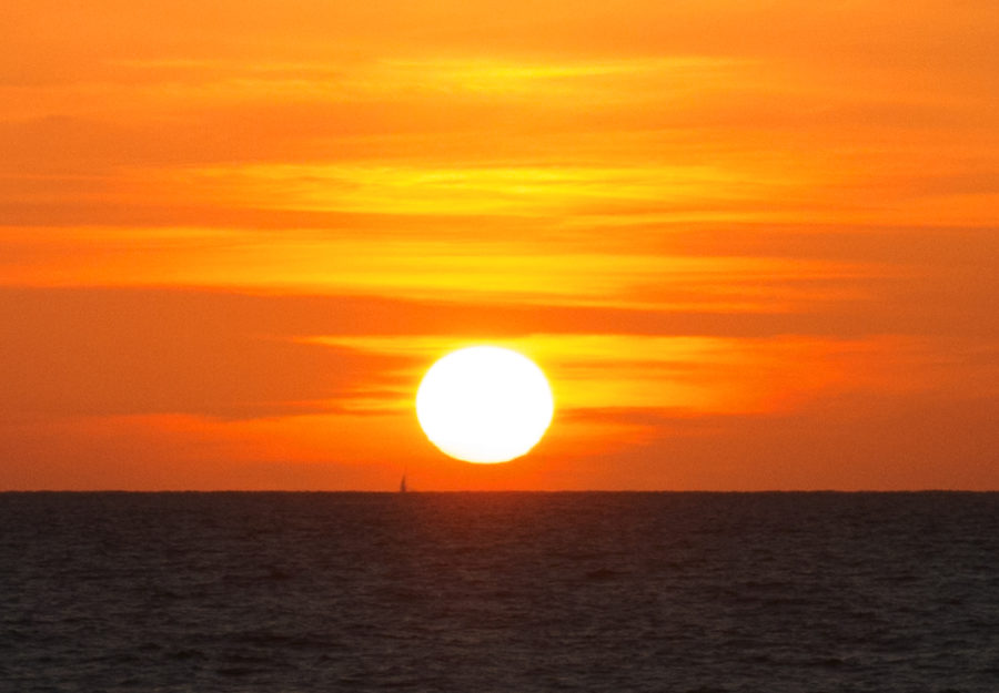 a round sun setting in the orange sky over a dark horizon 