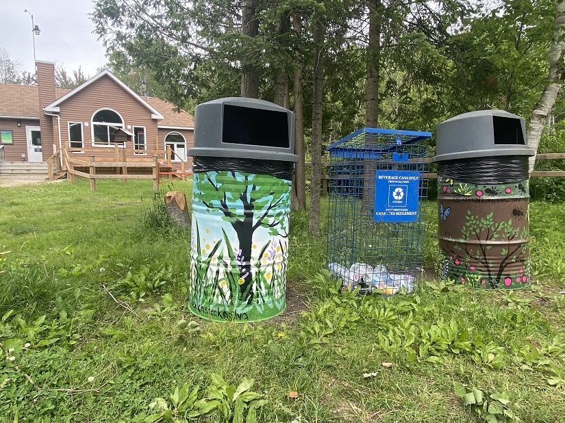 Two painted garbage barrels on grass in front of building. 