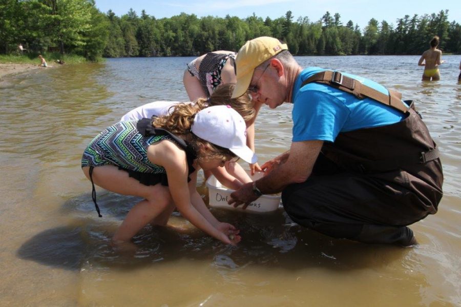 Scientist and two girls look at small creature while standing in river. 