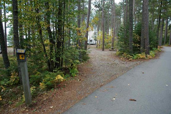 Paved road runs by pathway to campsite through trees. 