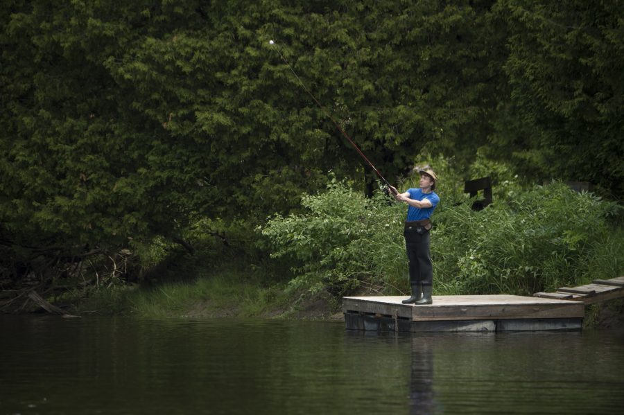 Man casts off a dock wearing fishing waders. 