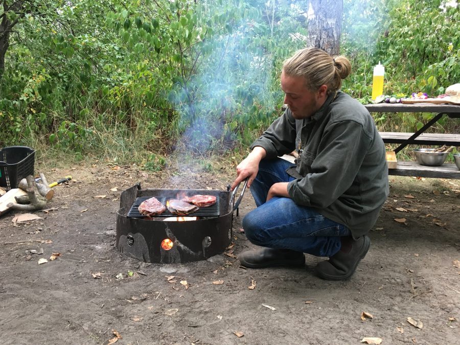 Chef Lucan kneeling beside fire while grilling ribeye steak