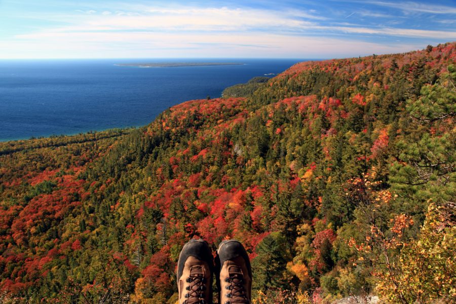 hiker looking down from lookout at rolling hills of fall foliage over Lake Superior