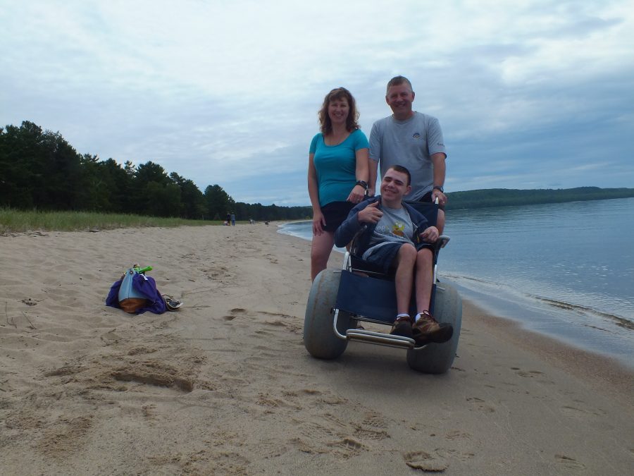 man in large-wheeled chair with family members on beach