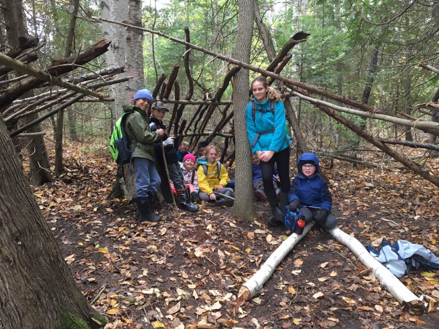 Kids stand in forest with makeshift shelters
