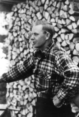 Black and whit photo of man in front of logs