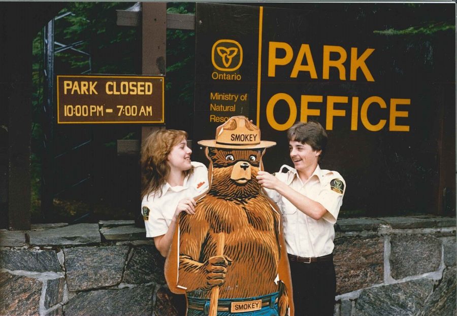 a male and a female gate attendant pose with Smokey the Bear statue 