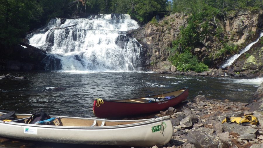 2 canoes on a rock shore, with waterfall in the background
