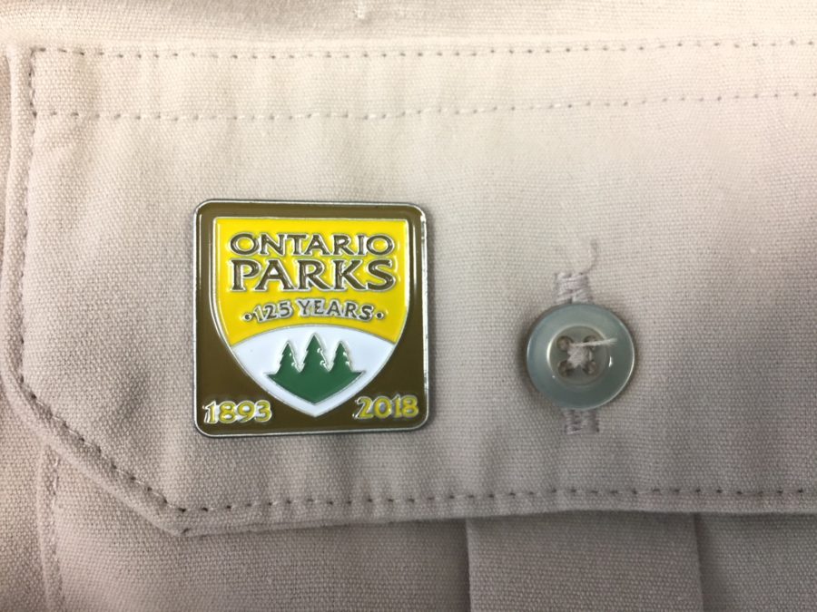 small metal pin on the fonrt pocket of a beige parks shirt that says, Ontario Parks, 125 years, 1893 2013