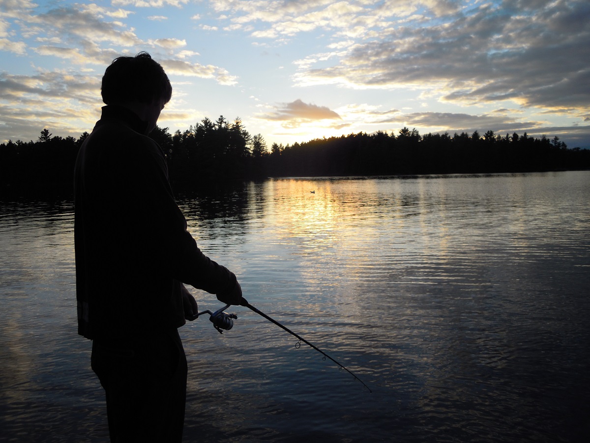 Un pêcheur pêchant dans un lac au coucher du soleil