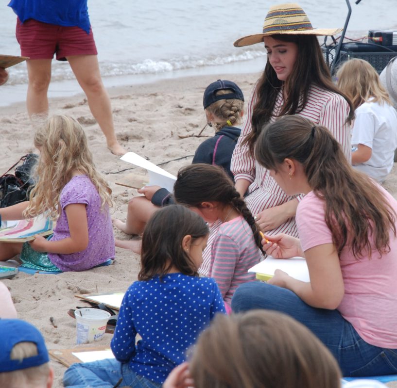 children painting on beach with teacher
