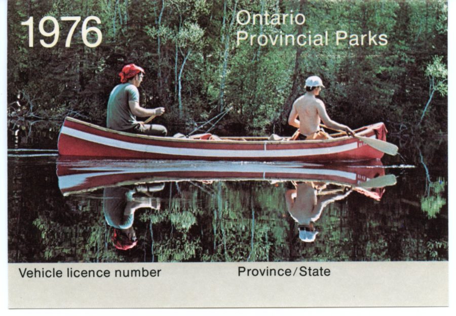 Photo de deux hommes dans un canot rouge avec une bande blanche qui navigue sur l’eau dans laquelle on peut voir leur réflexion. Les hommes ne portent pas de VFI. Les mots suivants sont disposés sur le permis : «?1976, Parc provincial de l’Ontario, Plaque d’immatriculation du véhicule, Province/État?»