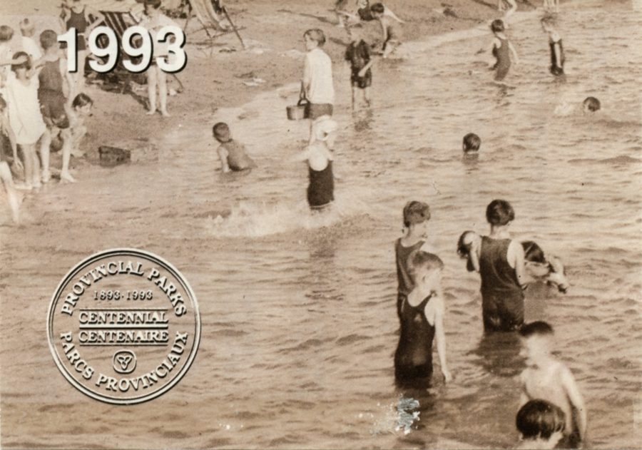 Black and white photo of kids on the beach from the 1920's or 1930's. There is a circle on the image that states Provincial Parks 1893 - 1993 Centennial Centenaire Parcs Provinciaux"