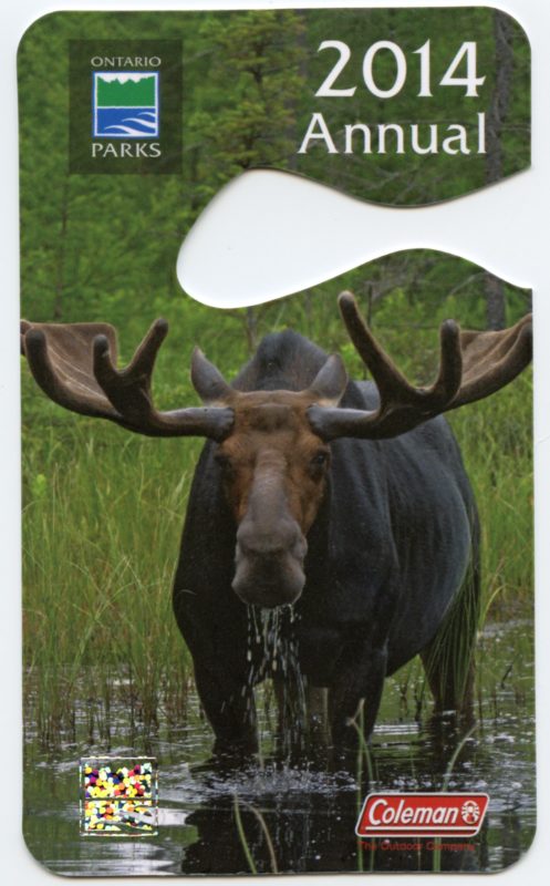 Image of a park pass of today that could fit on your rear view mirror. Photo on pass is of a bull moose in a wetland, looking directly at the camera. Logos are Ontario Parks and Coleman and text says 2014 Annual. In the left corner there is a placeholder space for a hologram. 