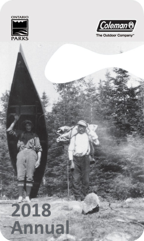 Image of the current park pass shape that fits over a rear-view mirror. Photo on pass shows two men, who look like they're from the early 1900's, one portaging a canoe, and the other with a large pack, with trees in the background. Logo's depicted are Ontario Parks and Coleman. Text states: "2018 Annual". 