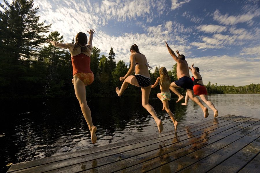 Cinq personnes sautant d’un quai dans l’eau (prise de vue de derrière)