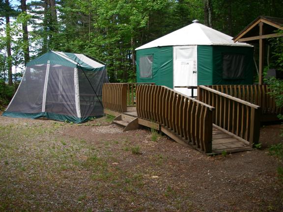 Green yurt with white roof, with deck and dining tent around the picnic table