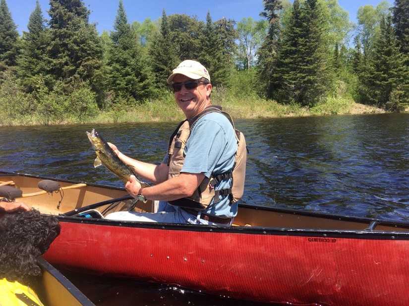 Man sitting in canoe holding fish.
