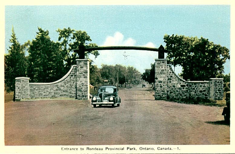 Postcard with old stone gates originally at the entrance to Rondeau, with an old timey car driving through, looks like the 50's. 
