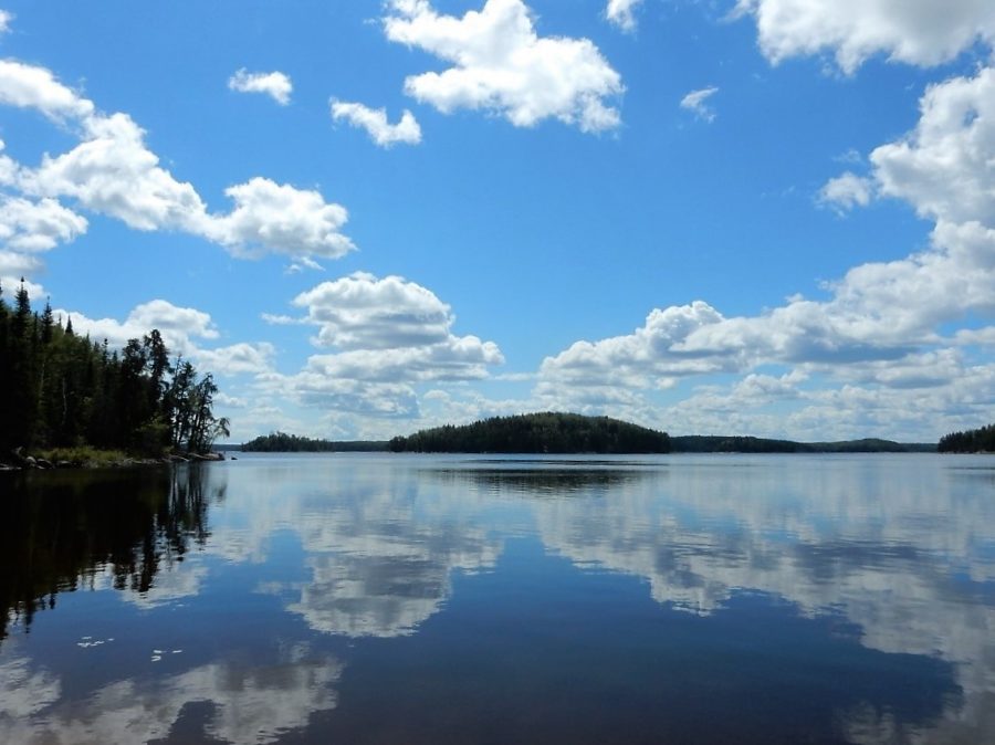 Picture of a lake reflecting the blue sky with white clouds, surrounded by coniferous trees