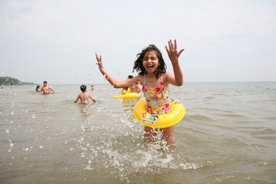Little girl, with a floaty device around her waist, splashing in the lake and having a blast
