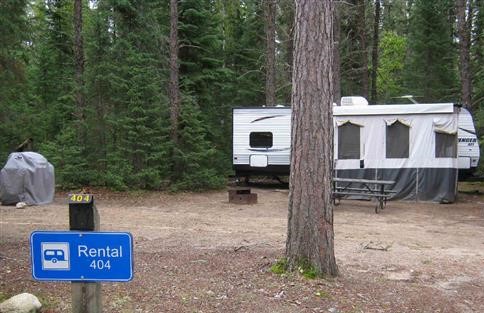 White trailer sitting on campsite with a blue sign in the foreground saying "rental 404."