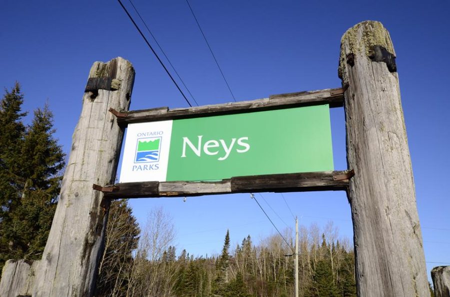 Panneau de signalisation vert indiquant Neys, avec le logo de Parcs Ontario, soutenu par deux grands rondins, par un après-midi ensoleillé d’hiver.