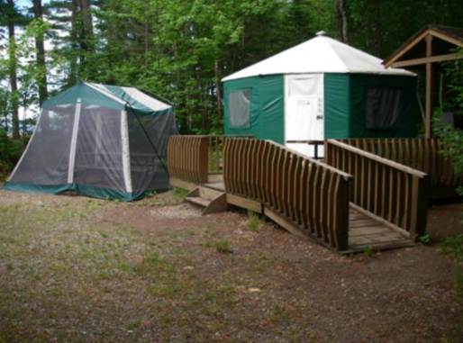 Green yurt with ramp and small porch. Picnic table is enclosed with a dining tent