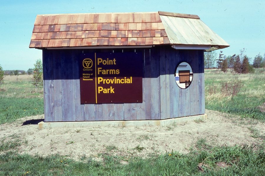 Panneau de signalisation brun de la province de l’Ontario avec l’ancien logo, indiquant Point Farms Provincial Park, appliqué sur des planches de grange et couvert de bardeaux de bois.