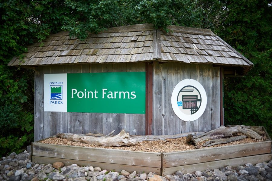 Panneau de signalisation vert de Parcs Ontario avec le logo, indiquant Point Farms, appliqué sur une structure faite de planches de grange et de bardeaux de bois.