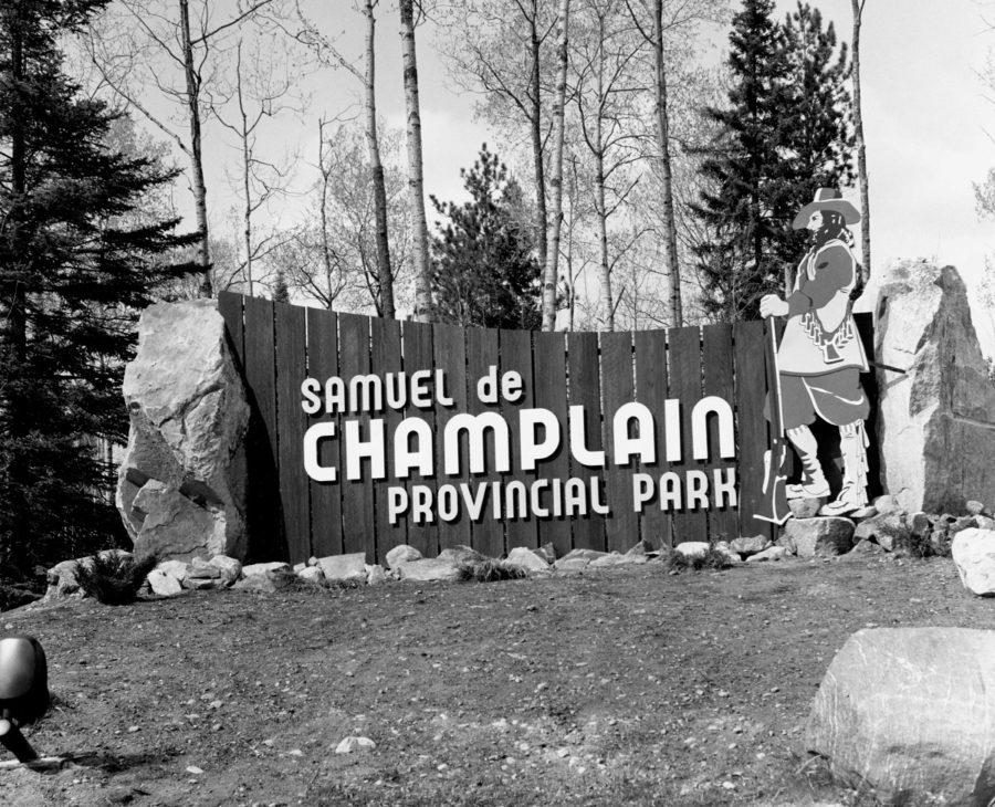 Black and white photo of Samuel de Champlain front gate sign with the explorer depicted to the side of the sign