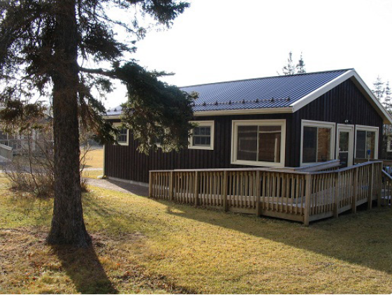 Exterior shot of small, dark brown cabin with white trim. Includes a wooden ramp up to front door
