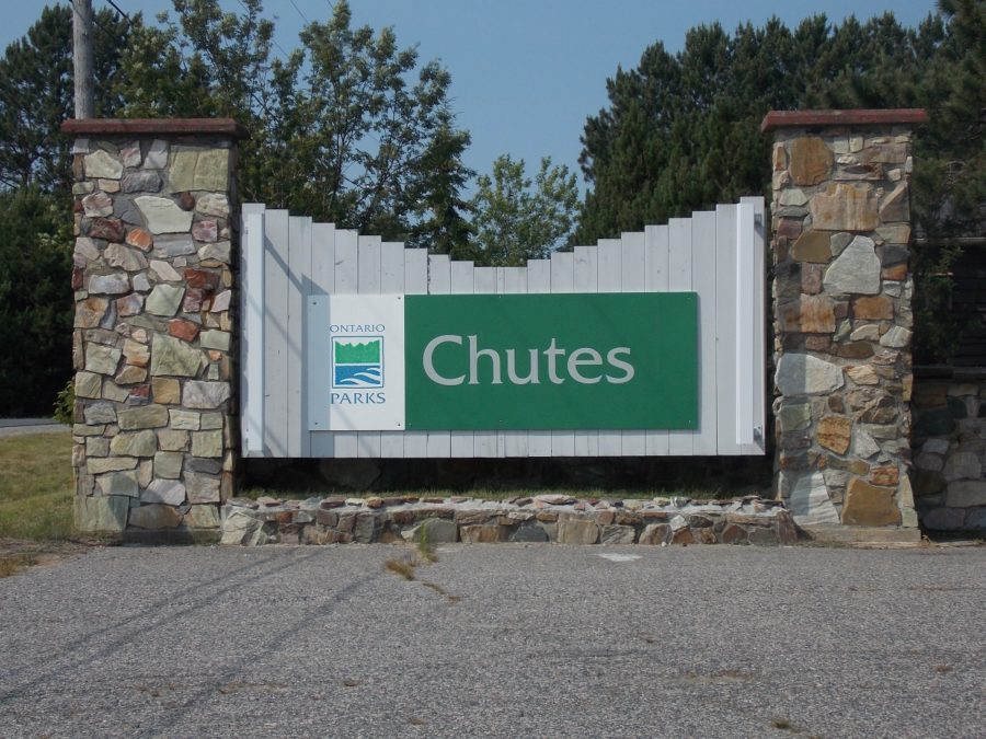 Panneau de signalisation vert avec le logo de Parcs Ontario appliqué sur un fond blanc, flanqué de deux piliers de pierre.