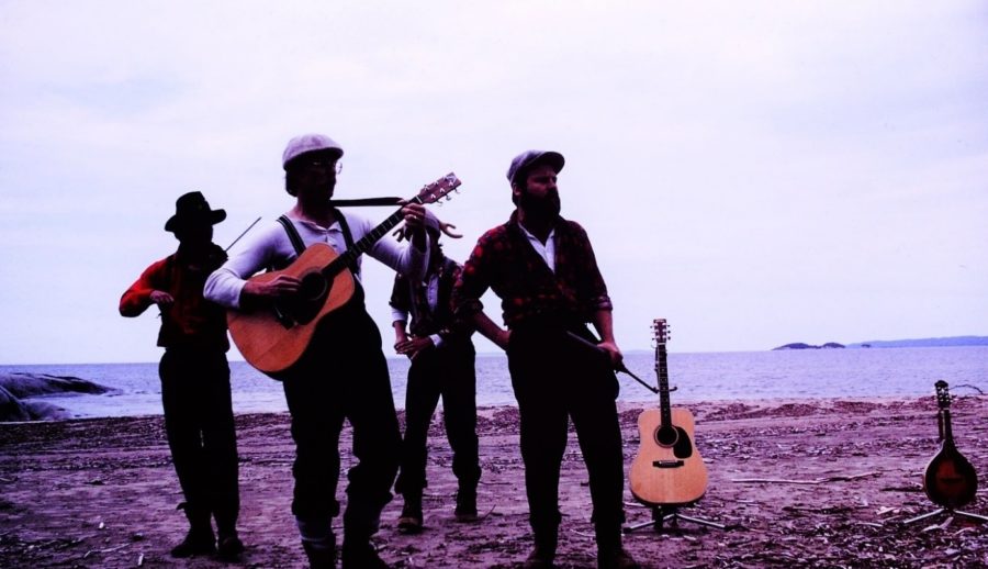 Four people, backlit, with instruments, standing on a beach