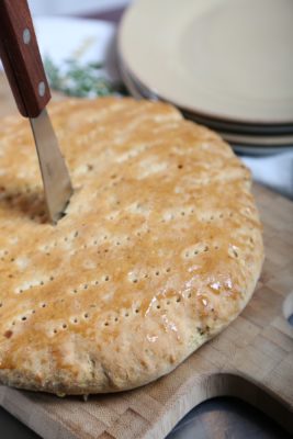 Round bread with tiny holes (from fork), on a cutting board with a butter knife sticking out of it