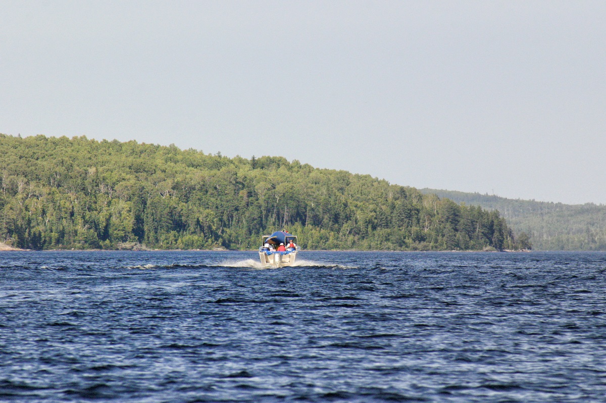 Le lac bleu avec un bateau s’éloignant du photographe, le ciel gris et la forêt en arrière-plan.