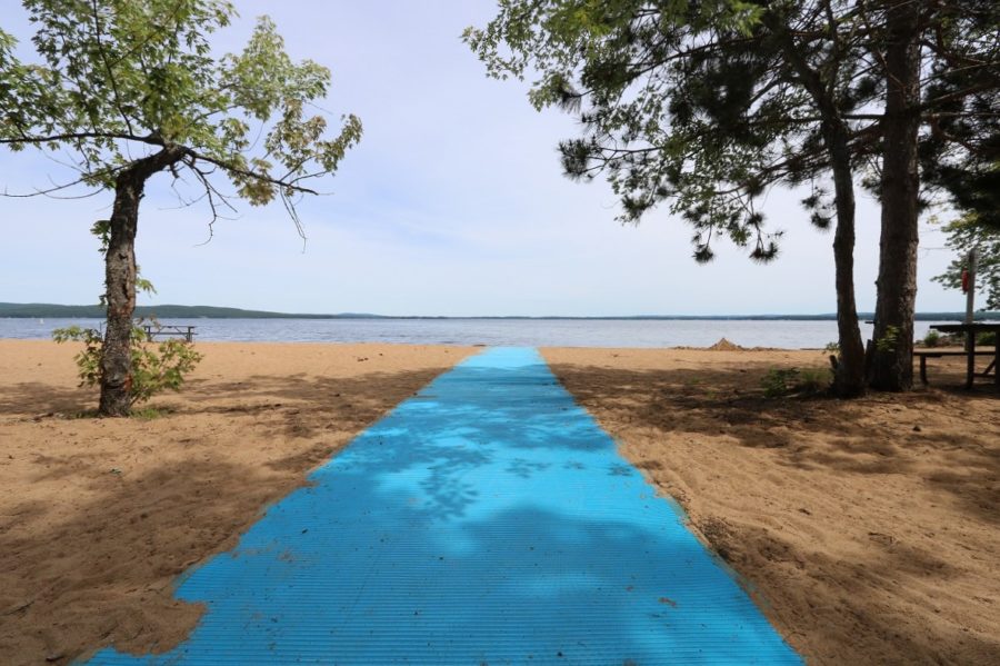 Large voie piétonnière bleu pâle sur une plage de sable menant à l’eau