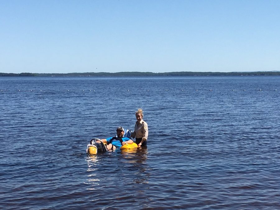 Homme utilisant un fauteuil amphibie WaterWheels sur l’eau, accompagné d’un membre du personnel du parc