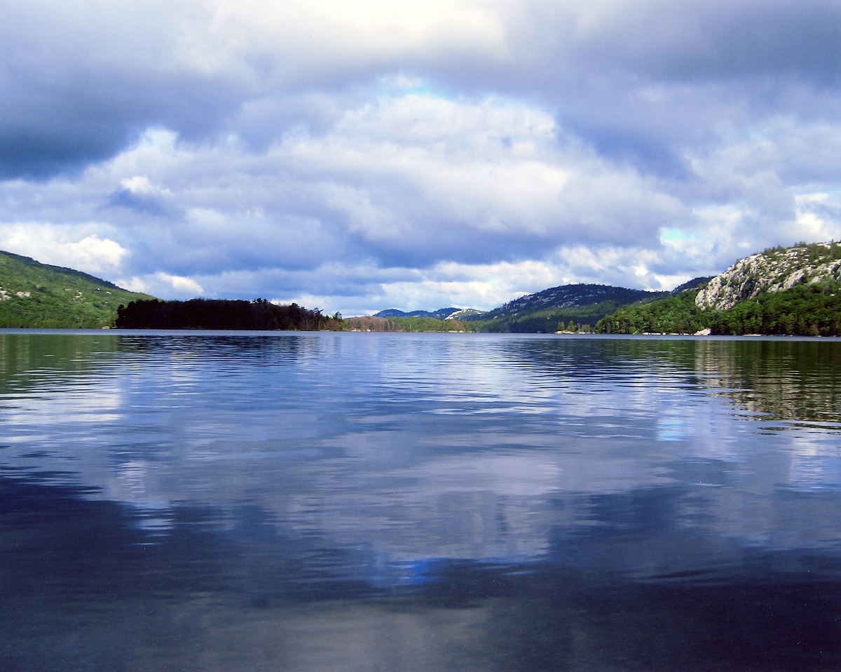 Un lac qui reflète les nuages du ciel avec des formations géologiques et une forêt entourant le lac