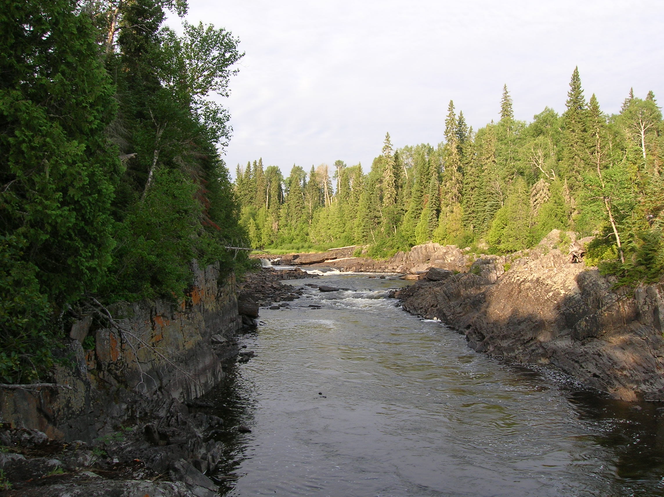 Une rivière traversant une rive en rochers en parallèle à la forêt boréale