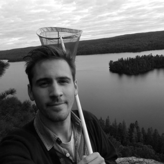 Selfie of a man with a net over his shoulder with a lake and forest in the background - black and white photo