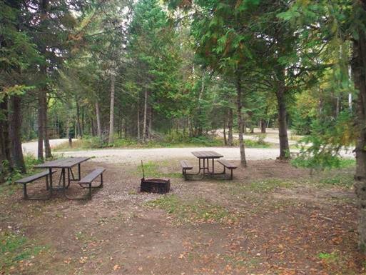 Grand site sur une boucle du sentier, avec aménagement pour feu de camp et tables de pique-nique.