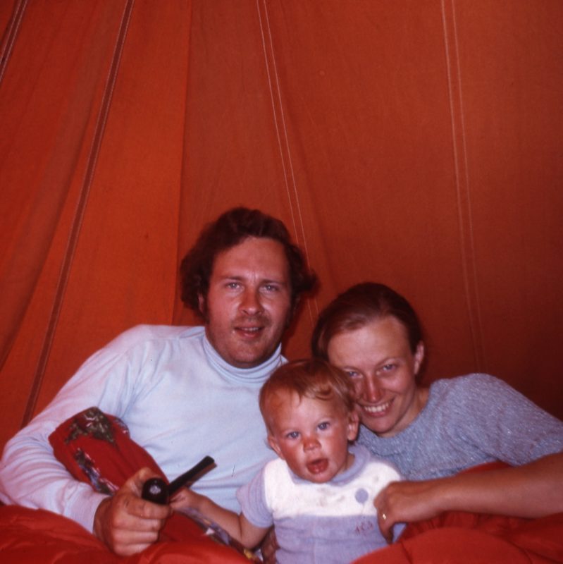 Family of three, posing in the 70s with an orange backdrop (orange tent)