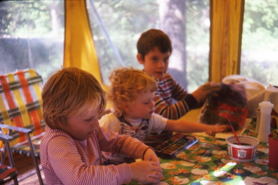 Three kids, engaged in activity, in a meal tent in the 70s